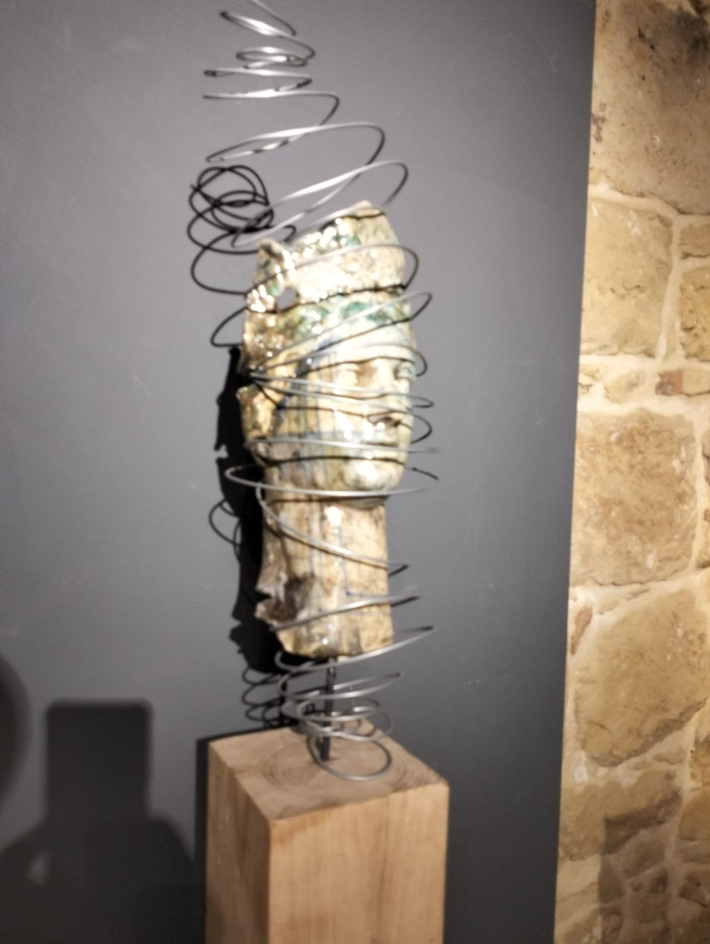 Volto Raku avvolto da spire metalliche su base in legno