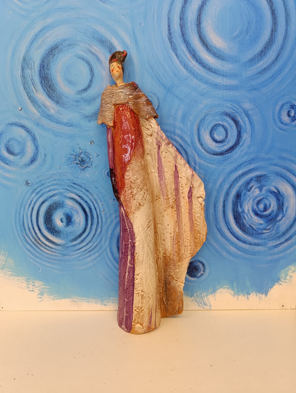 Figura femminile in ceramica con mantello su fondo azzurro a spirali